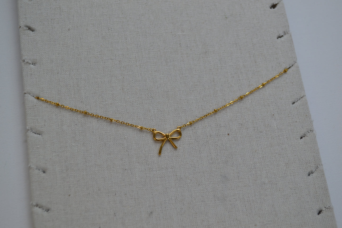 Gouden ketting met een gouden strik bedel op een beige ketting stand.