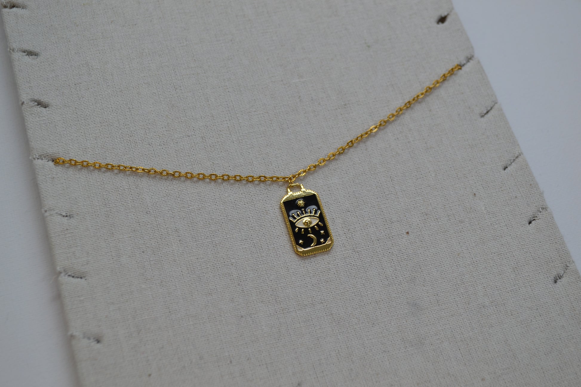 Gouden ketting met een zwart met gouden bedel op een beige ketting stand.