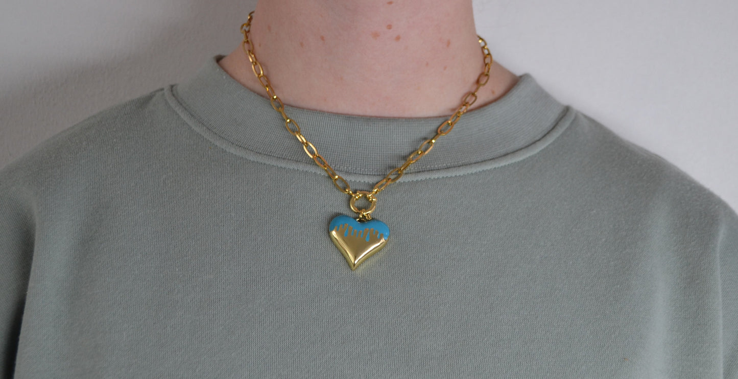 Gouden ketting met een gouden en blauwe hart bedel om de nek van een persoon.