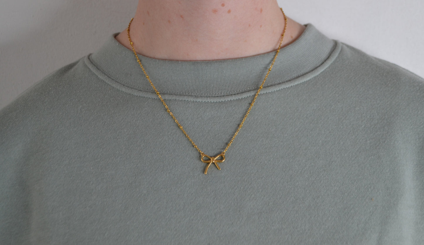 Gouden ketting met een gouden strik bedel. Een vrouw heeft de ketting om.