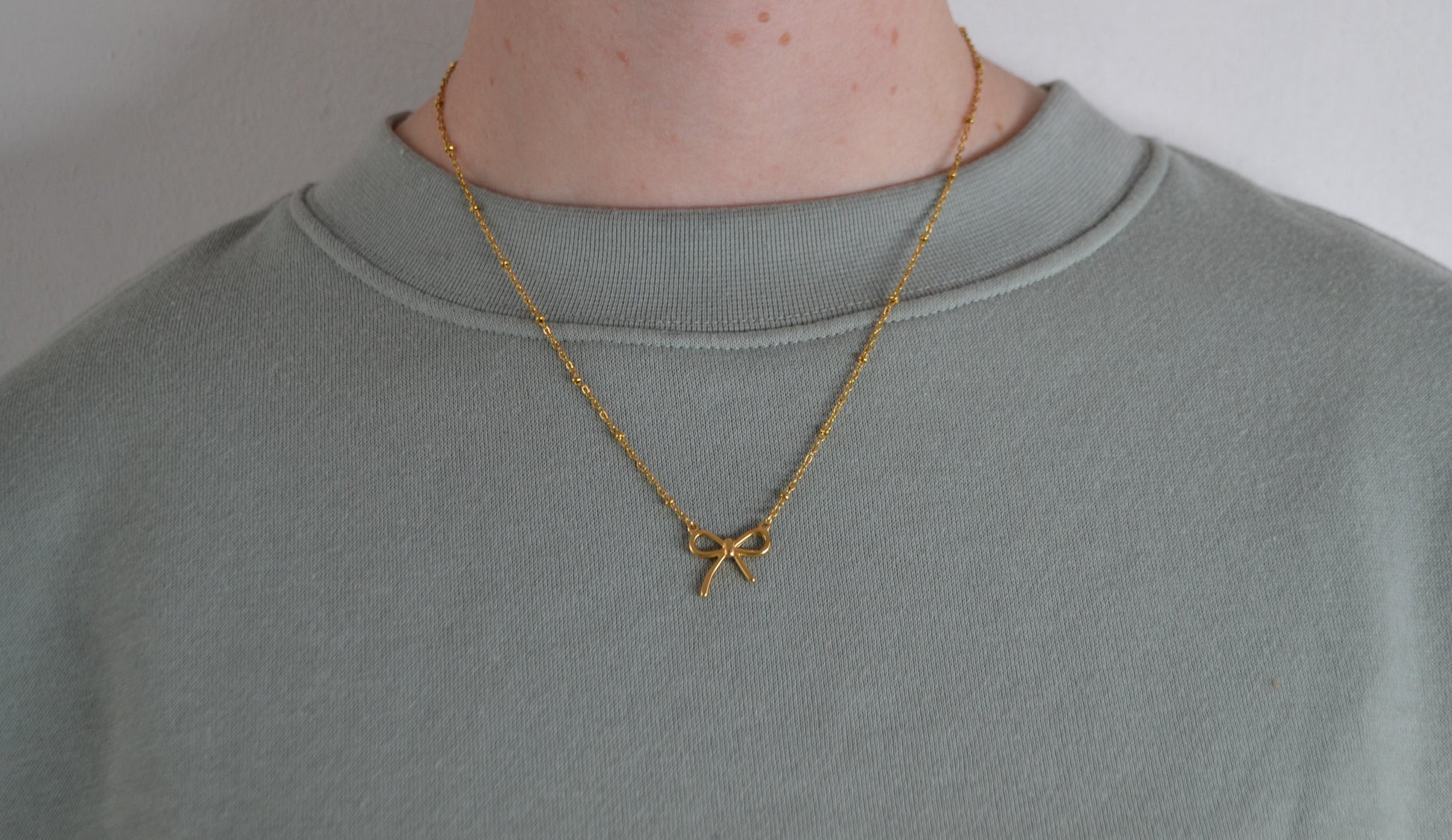 Gouden ketting met een gouden strik bedel. Een vrouw heeft de ketting om.