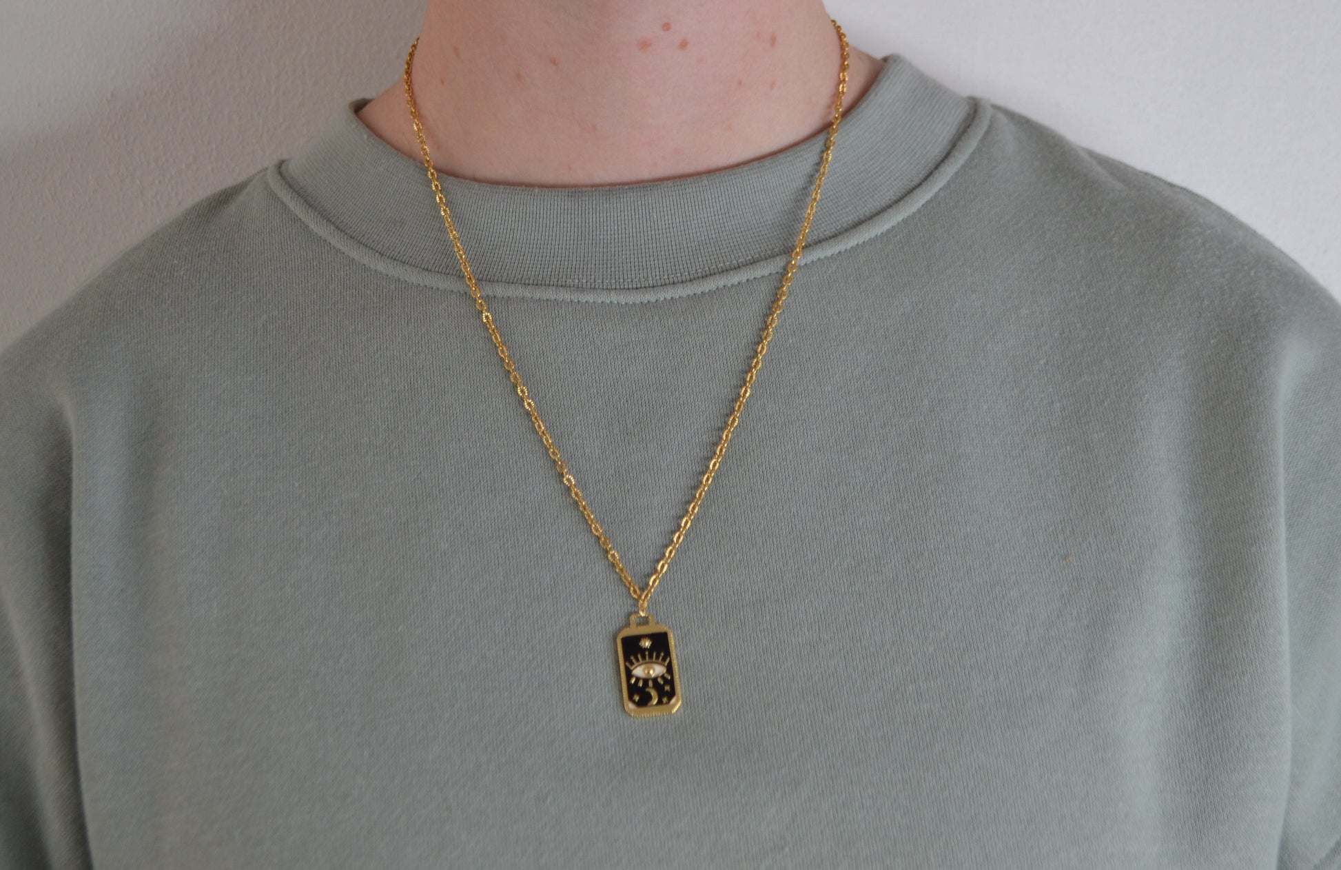 Gouden ketting met een zwart met gouden bedel  om de nek van een vrouw.