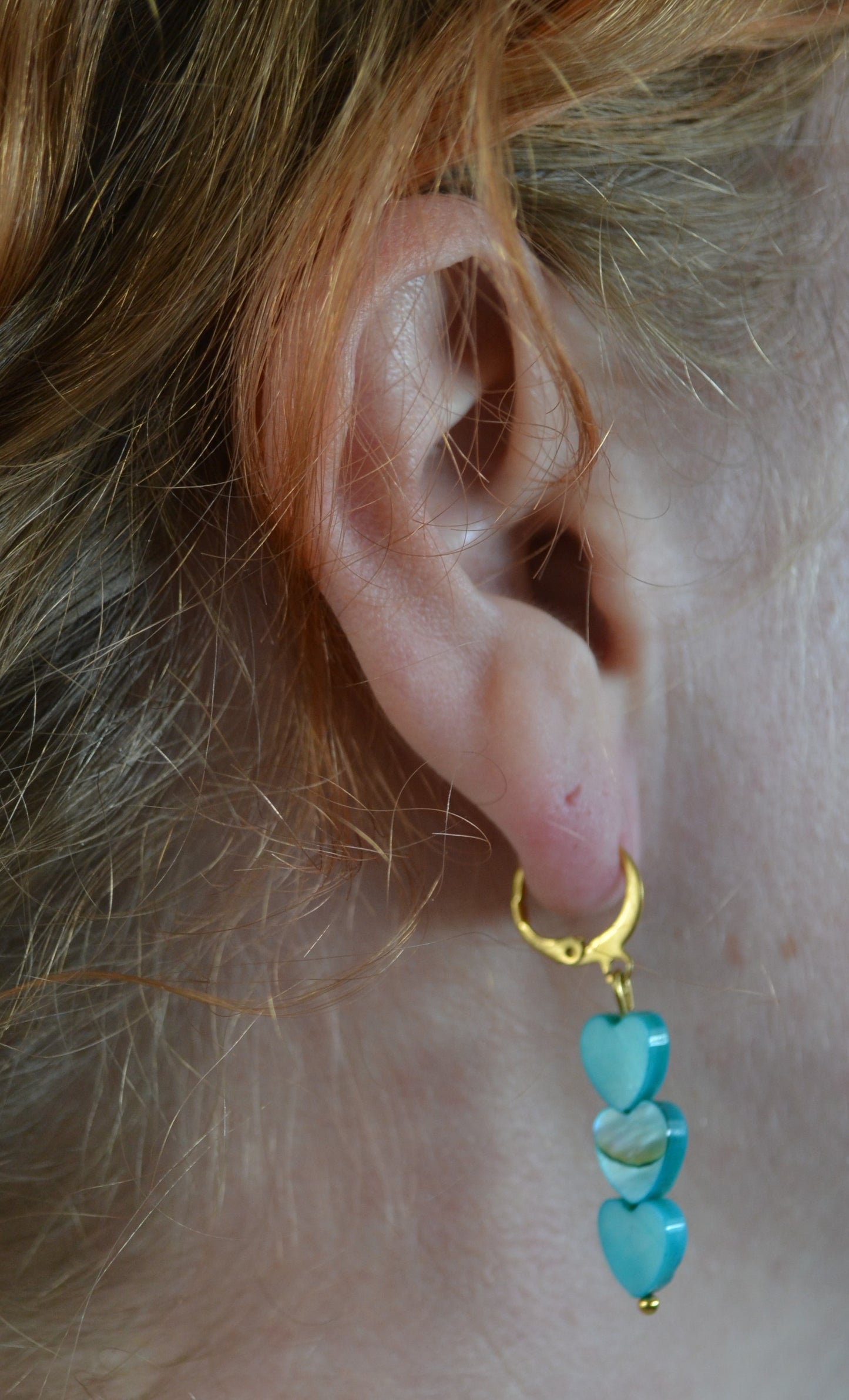 Oorbellen met een gouden clip en drie blauwe hartjes in de oren van een vrouw.