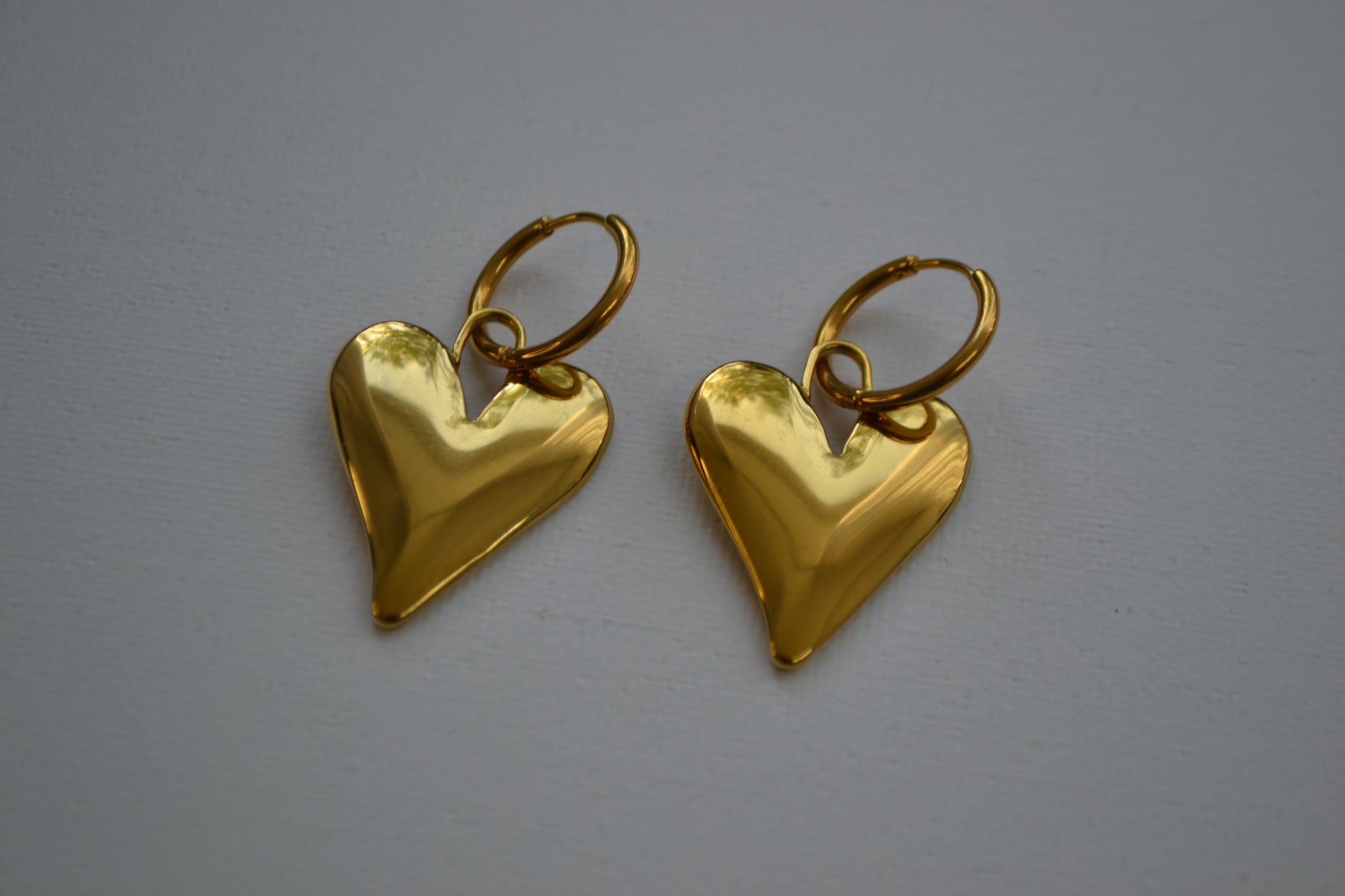 Gouden oorbellen met een creool en een grote bedel in de vorm van een hart. Op een witte achtergrond.