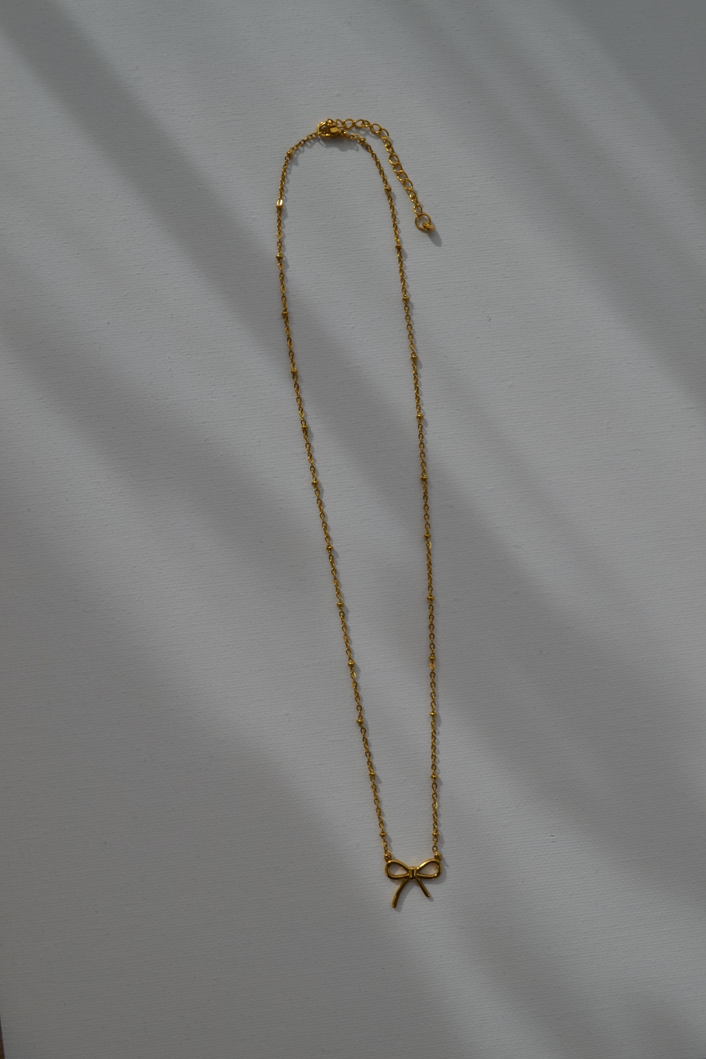 Gouden ketting met een gouden strik bedel op een witte achtergrond.