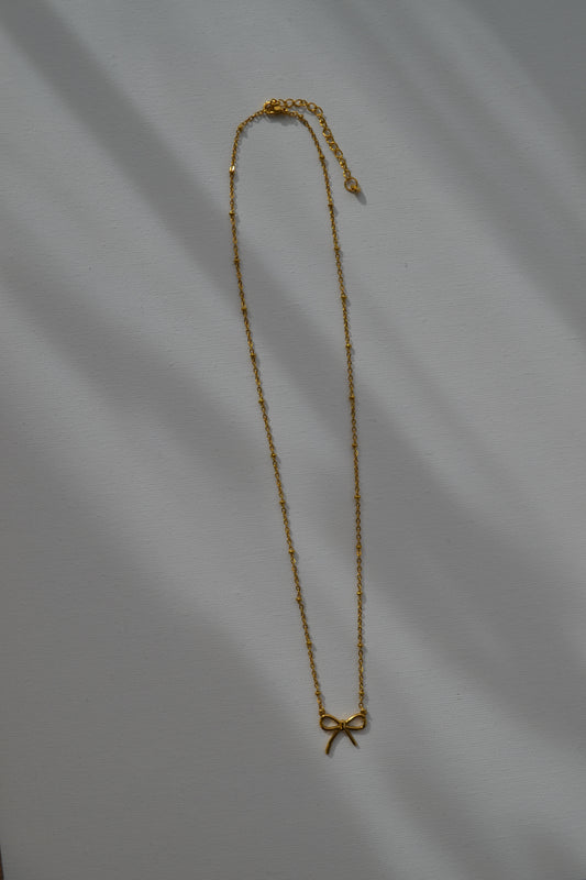 Gouden ketting met een gouden strik bedel op een witte achtergrond.