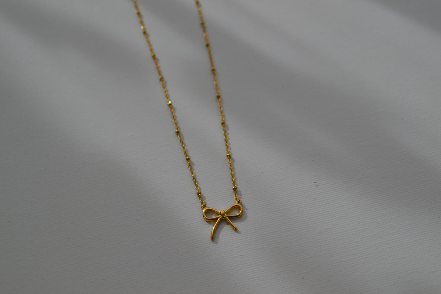 Gouden ketting met een gouden strik bedel op een witte achtergrond. De foto zoomed in op de bedel.