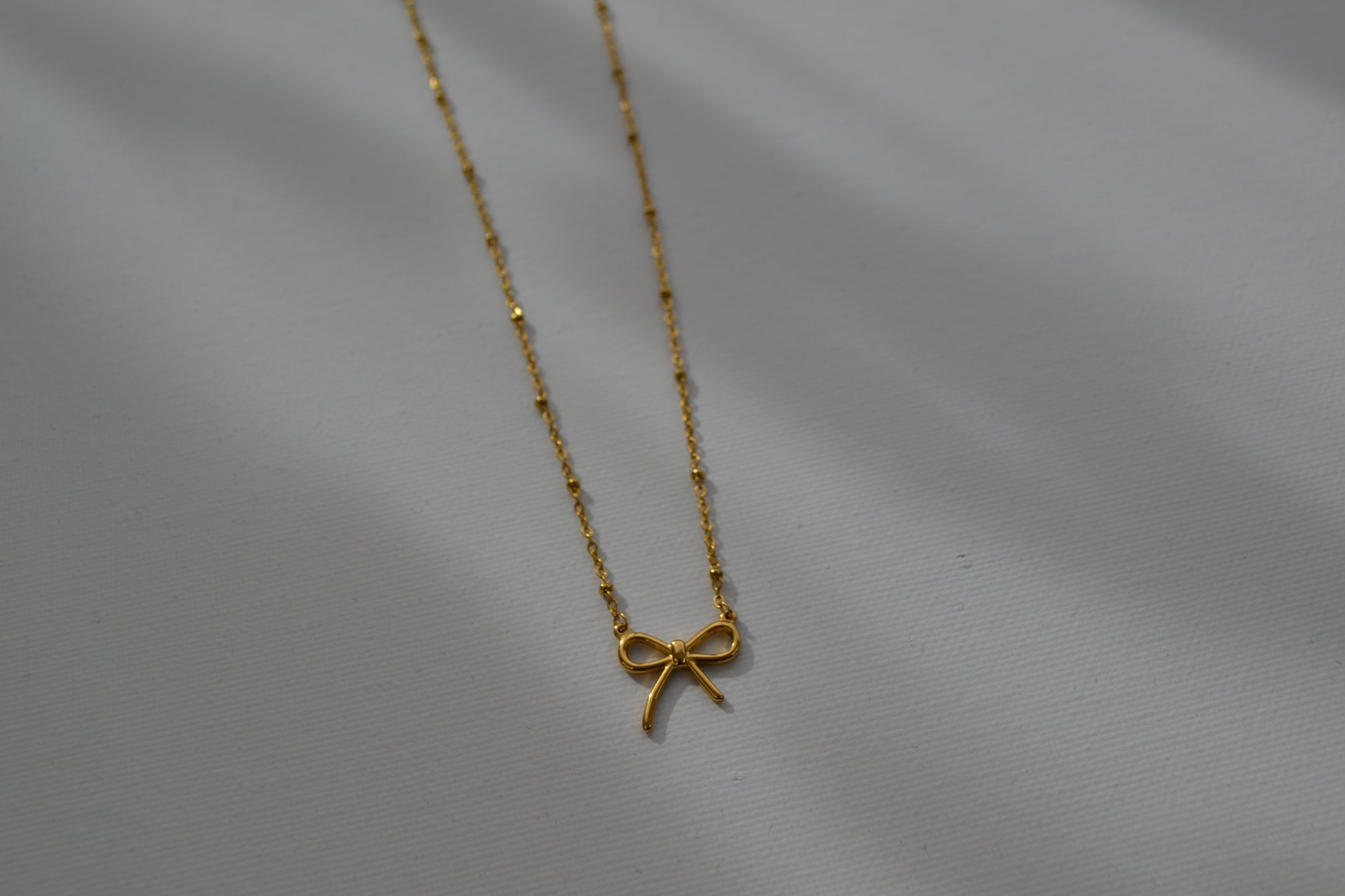 Gouden ketting met een gouden strik bedel op een witte achtergrond. De foto zoomed in op de bedel.