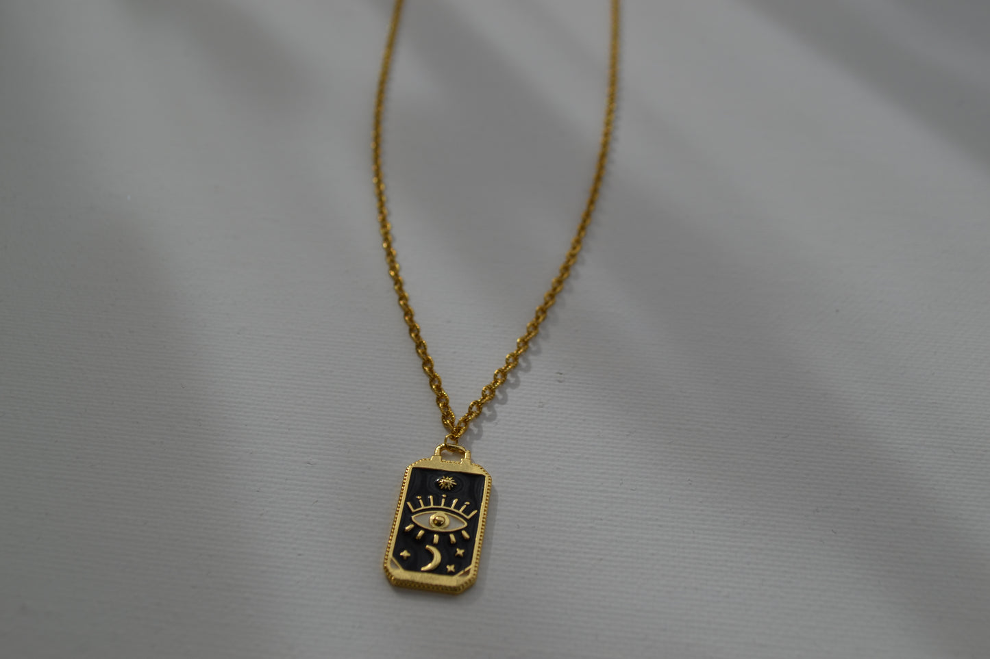 Gouden ketting met een zwart met gouden bedel, ingezoomed op de bedel en met een witte achtergrond.