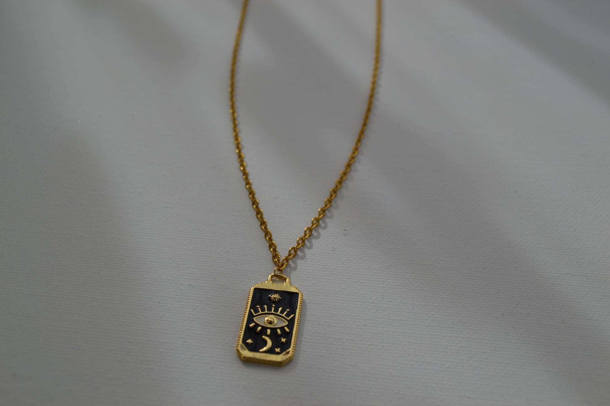 Gouden ketting met een zwart met gouden bedel, ingezoomed op de bedel en met een witte achtergrond.