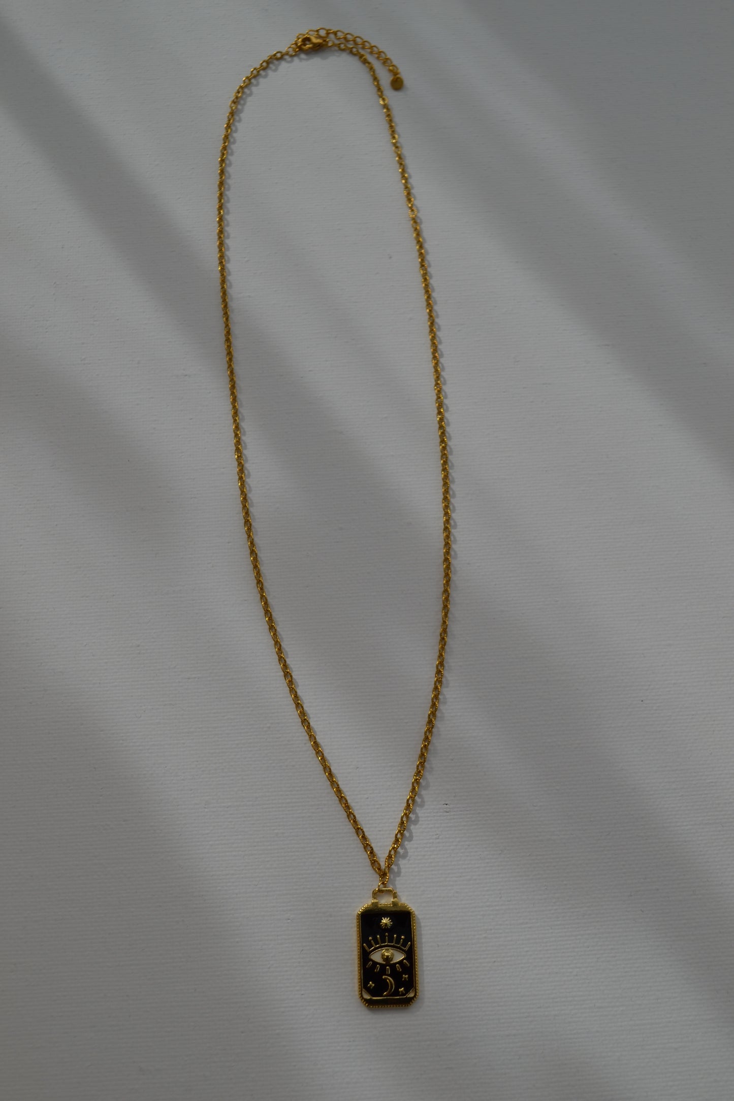 Gouden ketting met een zwart met gouden bedel op een witte achtergrond.