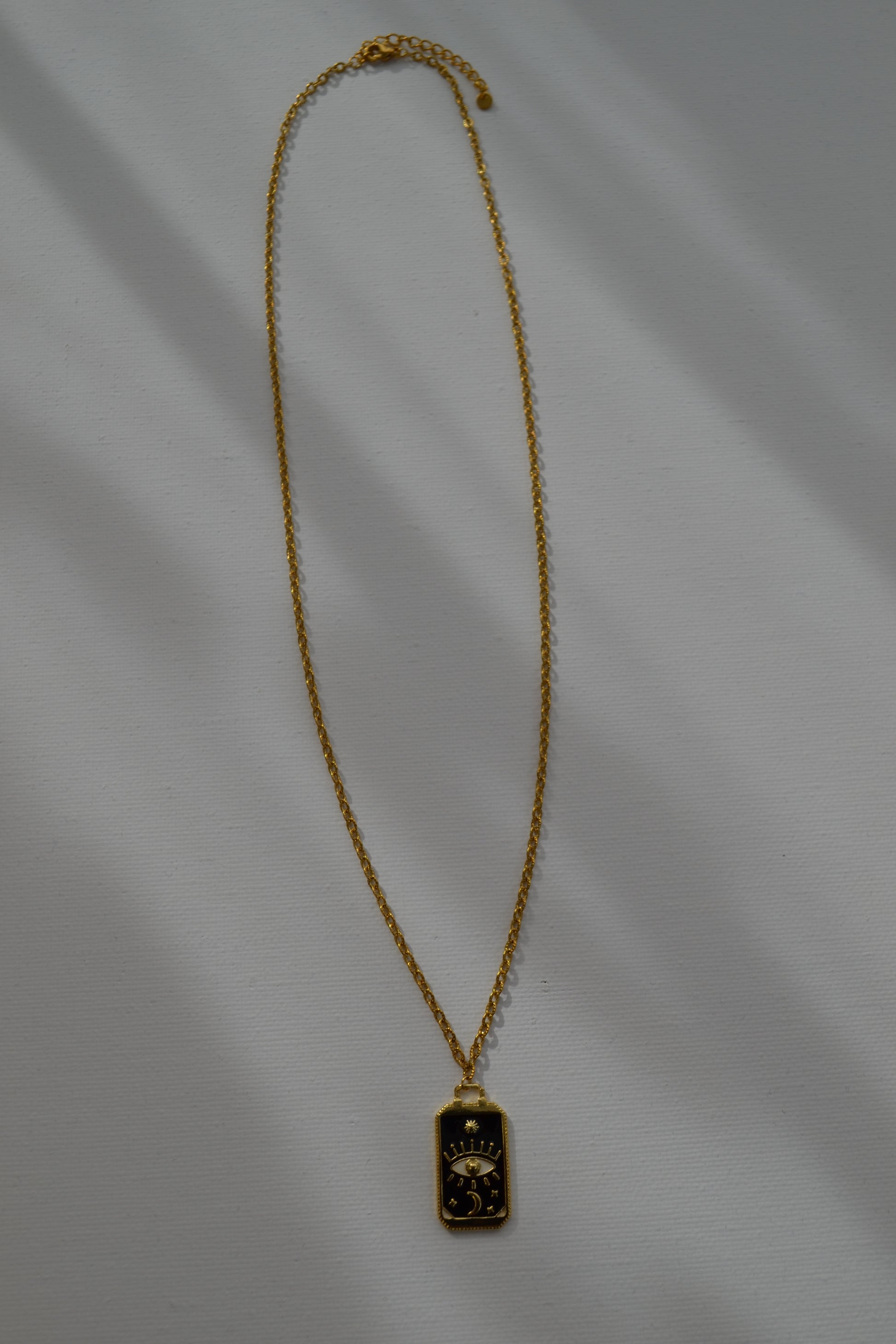 Gouden ketting met een zwart met gouden bedel op een witte achtergrond.