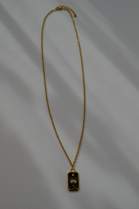 Gouden ketting met een zwart met gouden bedel op een witte achtergrond.