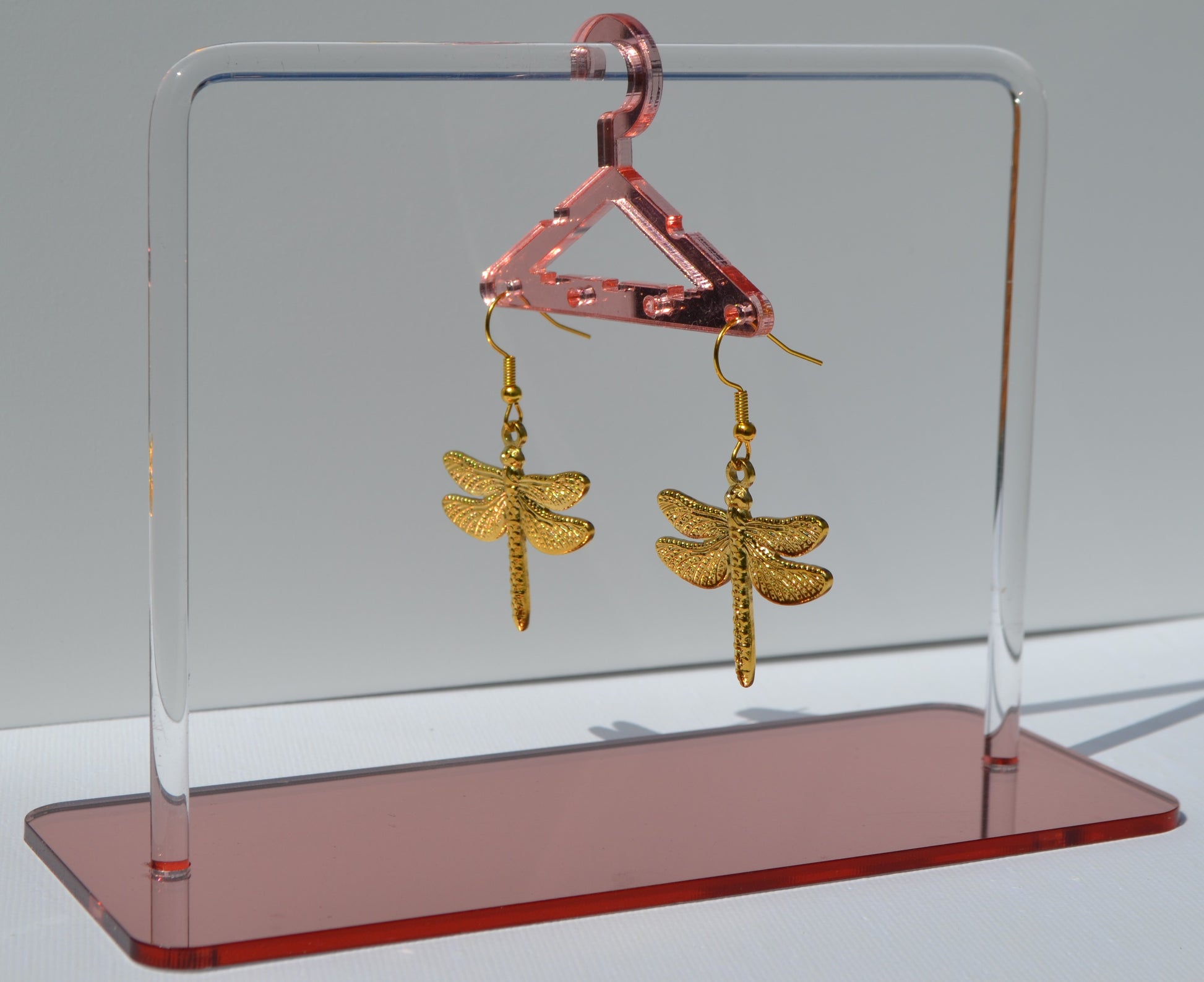 Gouden oorbellen met een haakje en een bedel in de vorm van een libelle die aan een rekje hangen.