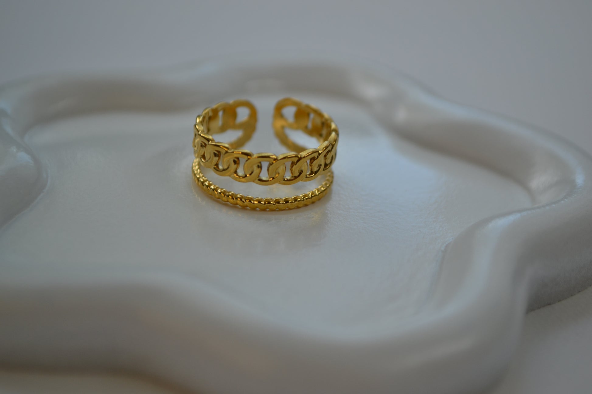 Gouden ring met een dubbele band op een wit bordje in de vorm van een bloem.