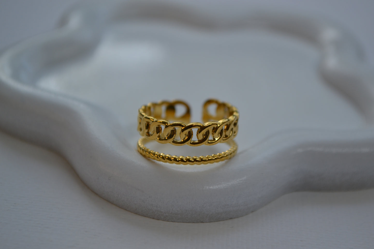 Gouden ring met een dubbele band op een wit bordje in de vorm van een bloem.