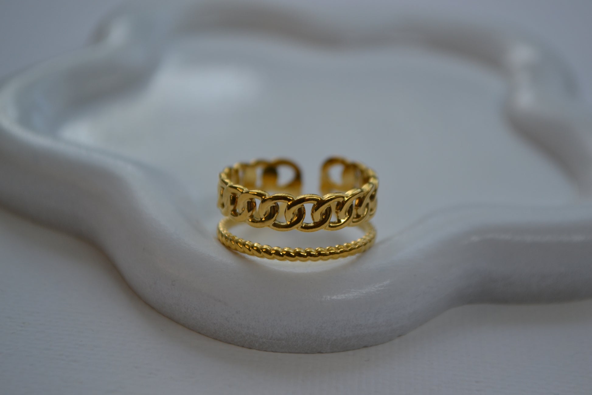Gouden ring met een dubbele band op een wit bordje in de vorm van een bloem.