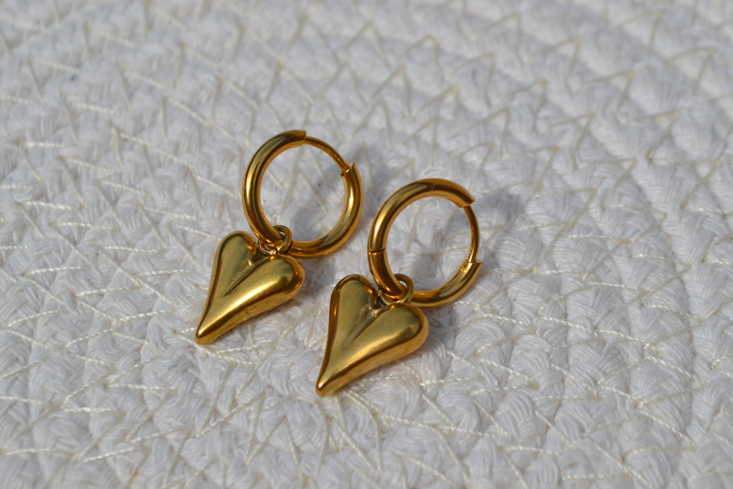 Oorbellen met gouden creoolen en een gouden bedel in de vorm van een hartje. De oorbellen liggen op een wit matje.