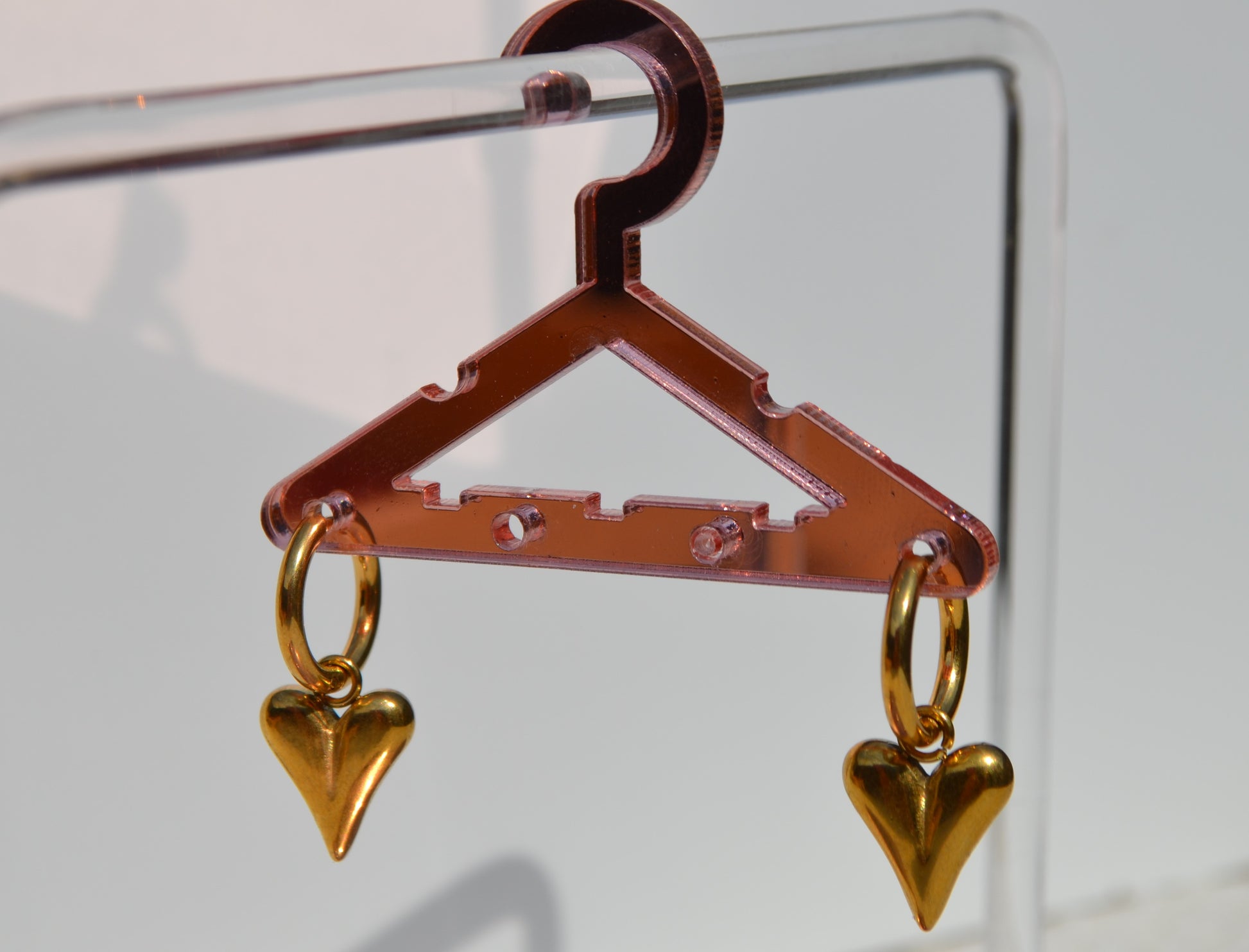 Oorbellen met gouden creoolen en een gouden bedel in de vorm van een hartje. De oorbellen hangen aan een roze rekje.